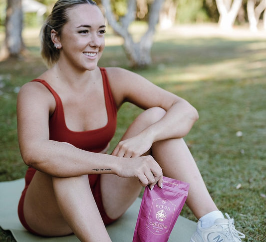 Woman sitting on an exercise mat in a park holding a pouch of Ritua Creatine for Women