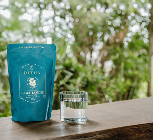 Pouch of Ritua L-Glutamine beside a glass of water on a timber bench