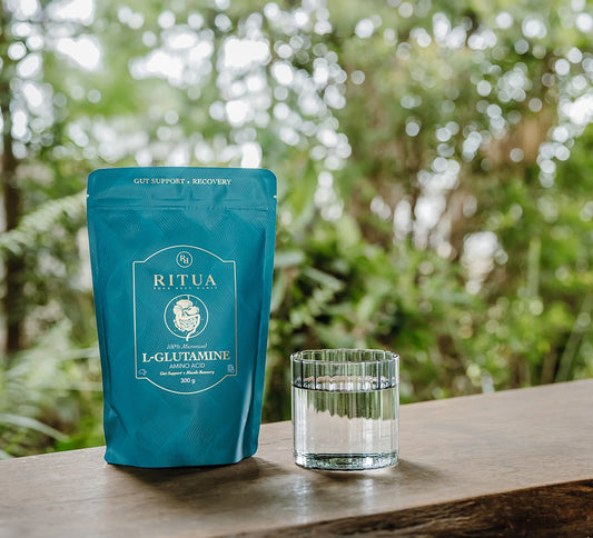 Pouch of Ritua L-Glutamine beside a glass of clear water on a timber bench