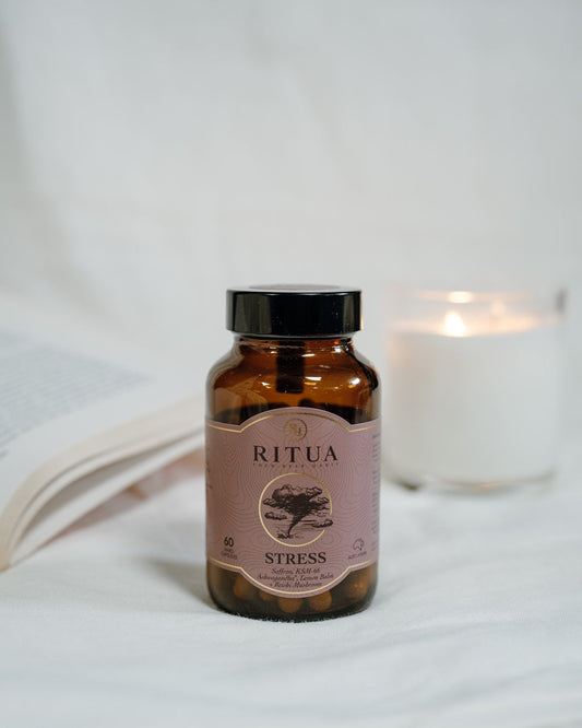 Bottle of Ritua Stress capsules on white linen beside an open book and a lit candle