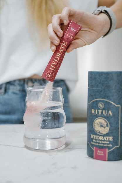 Ritua Hydrate Berry sachet mixing into a glass of water beside the tube
